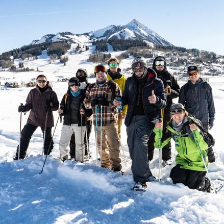 A group of showshoers posing for a photo in front of a mountain